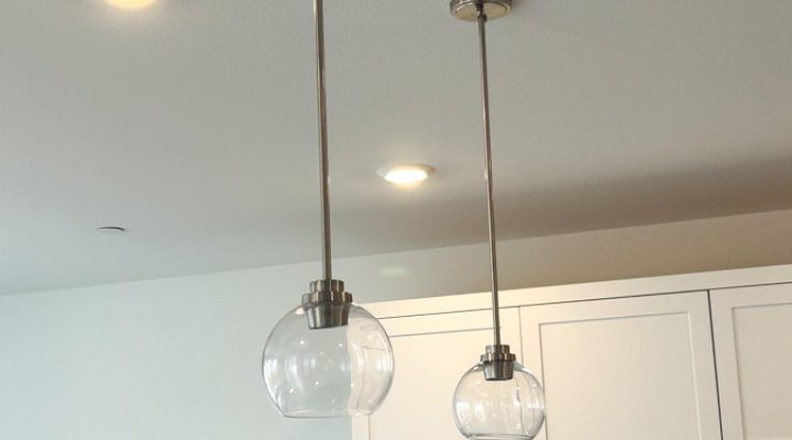 Two modern pendant lights hanging over a kitchen counter, enhancing the contemporary style with additional recessed lighting in the background.