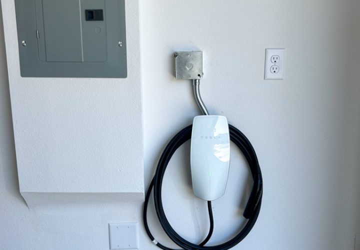 A Tesla home charger mounted on the garage wall next to the power switch, demonstrating a clean and efficient electric vehicle charging setup.